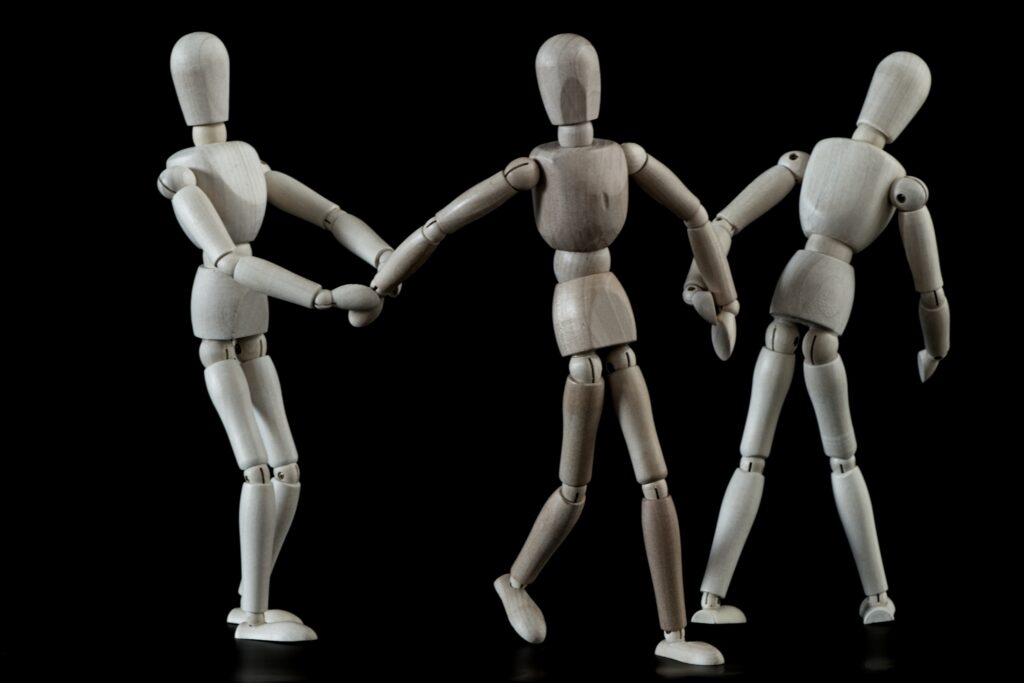 A wooden figure stands in the center while two others pull at her hands, representing Olivia and her alters vying for presence.